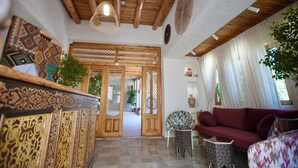 A traditional interior with wooden beams, a patterned wall, a sofa, and a chair. - Zargaron Boutique Hotel (Bukhara)