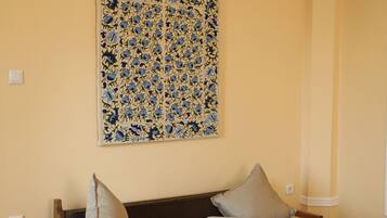 Una habitación con sofá de madera, cojines color crema y una obra de arte decorativa en la pared, además de un equipo de aire acondicionado.