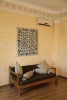Una habitación con sofá de madera, cojines color crema y una obra de arte decorativa en la pared, además de un equipo de aire acondicionado.
