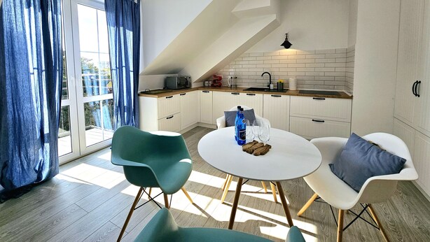 A modern kitchen with white cabinets, a black faucet, and a window with blue curtains. - Apartament Mundo Kołobrzeg - 365PAM (Kolobrzeg)