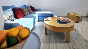 A living room with a blue sofa, a round wooden coffee table, and a bowl of fruit. - Apartament Mundo Kołobrzeg - 365PAM (Kolobrzeg)