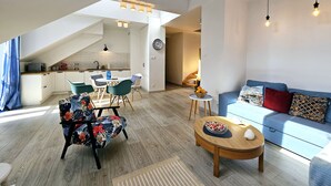 A modern living space with a dining area, kitchen, and a cozy seating area with a sofa and a coffee table. - Apartament Mundo Kołobrzeg - 365PAM (Kolobrzeg)