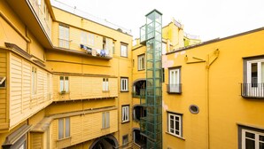 A multi-story yellow building with balconies, a central glass elevator shaft, and a narrow passageway. - Bisignano 11 in Naples (Naples)
