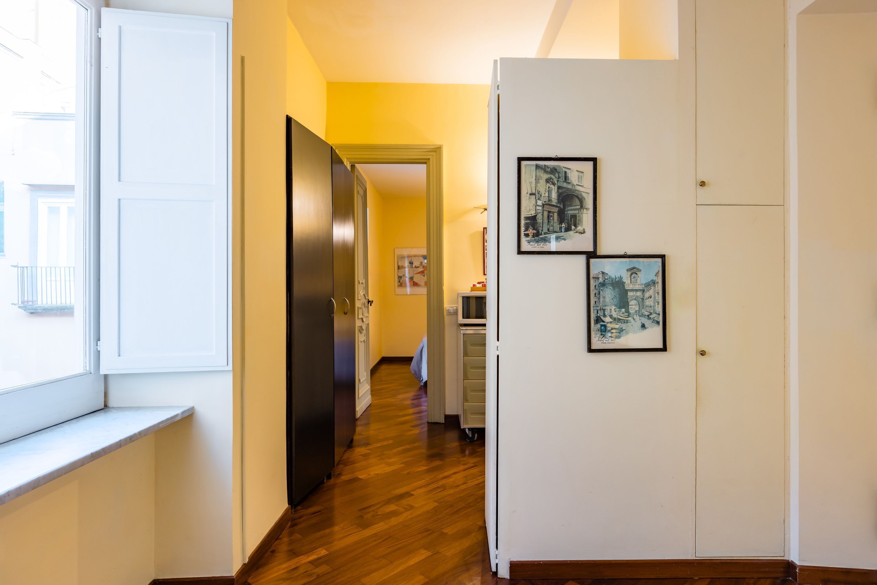 Un couloir avec un plancher en bois, une porte blanche et une armoire blanche ornée de deux tableaux encadrés.