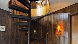 A spiral staircase with wooden steps and metal railings, leading to a landing with a wooden finish.
