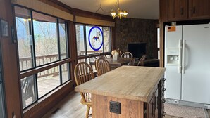 A kitchen with large windows, wooden furniture, a chandelier, and a white refrigerator.