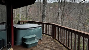A wooden deck with a hot tub and steps leading to a glass door.