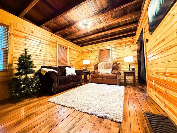 L’intérieur d’un chalet confortable, avec des murs en bois, une cheminée, deux canapés en cuir, un sapin de Noël et un grand tapis.