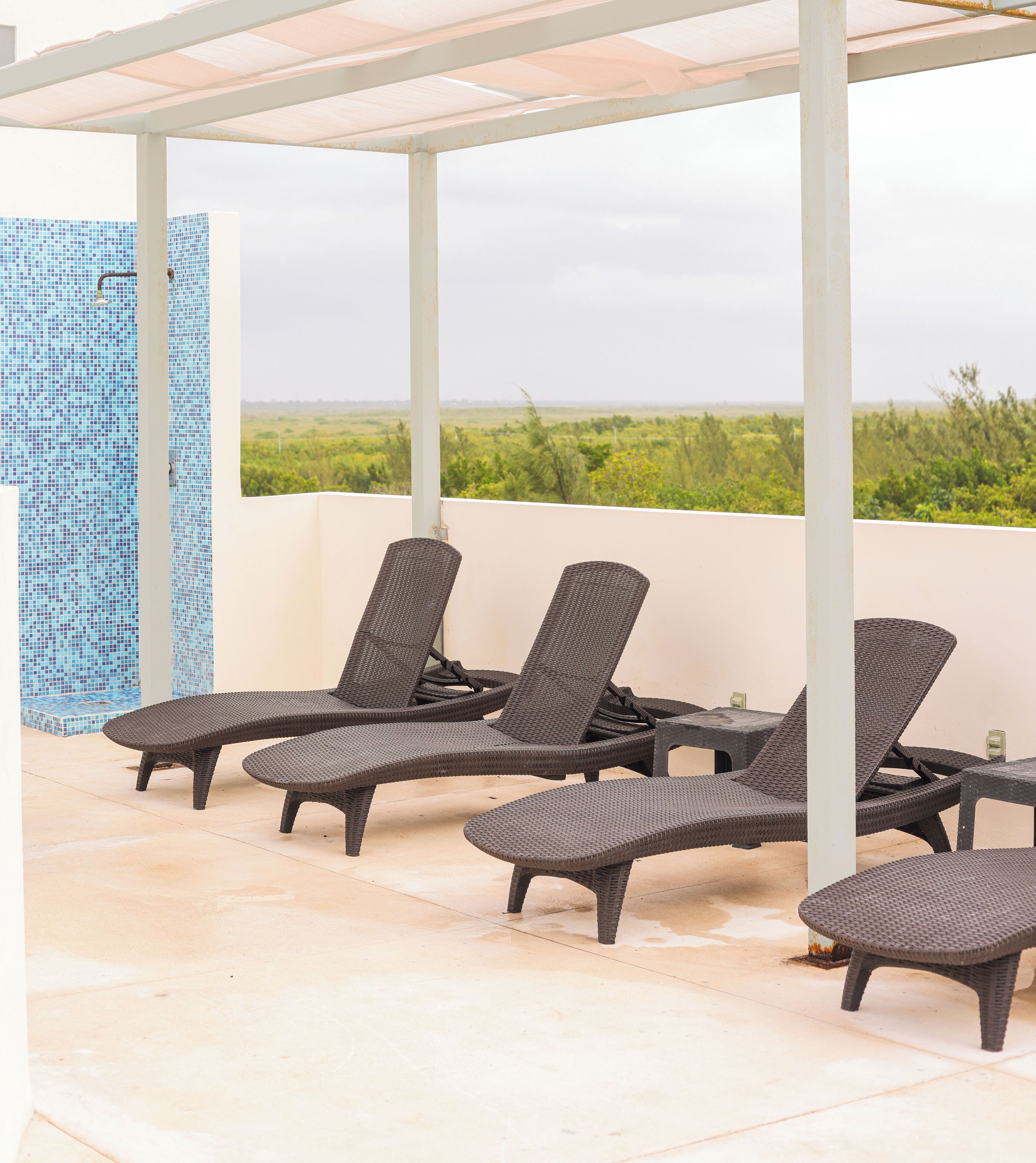 A covered outdoor seating area with lounge chairs and a tiled wall.