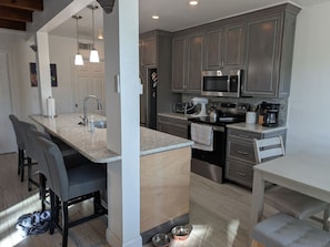 A modern kitchen with grey cabinets, a central island, and a dining area with grey chairs.