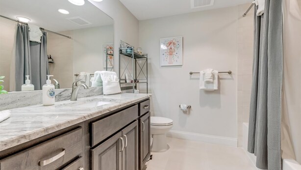 A modern bathroom with a large mirror, a shower, and a toilet. There are towels and toiletries on the counter. - Unit 203 Aruba - 3 Bedroom Ocean Front (Daytona Beach Shores)