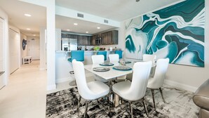 A modern kitchen with white cabinets, a central island, and a dining area with a marble table and white chairs. - Unit 203 Aruba - 3 Bedroom Ocean Front (Daytona Beach Shores)