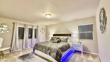 Un dormitorio con una cama grande, mesitas de noche, un tocador, un espejo, una ventana con persianas y una lámpara de techo.