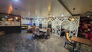 A restaurant with marble flooring, tables with chairs, decorative white panels, hanging pendant lights, and a modern ceiling design. - Hotel MK Vivanta (Gwalior)