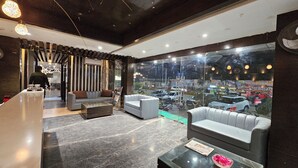 A modern lobby with a reception desk, seating area, and large windows offering a view of the street. - Hotel MK Vivanta (Gwalior)