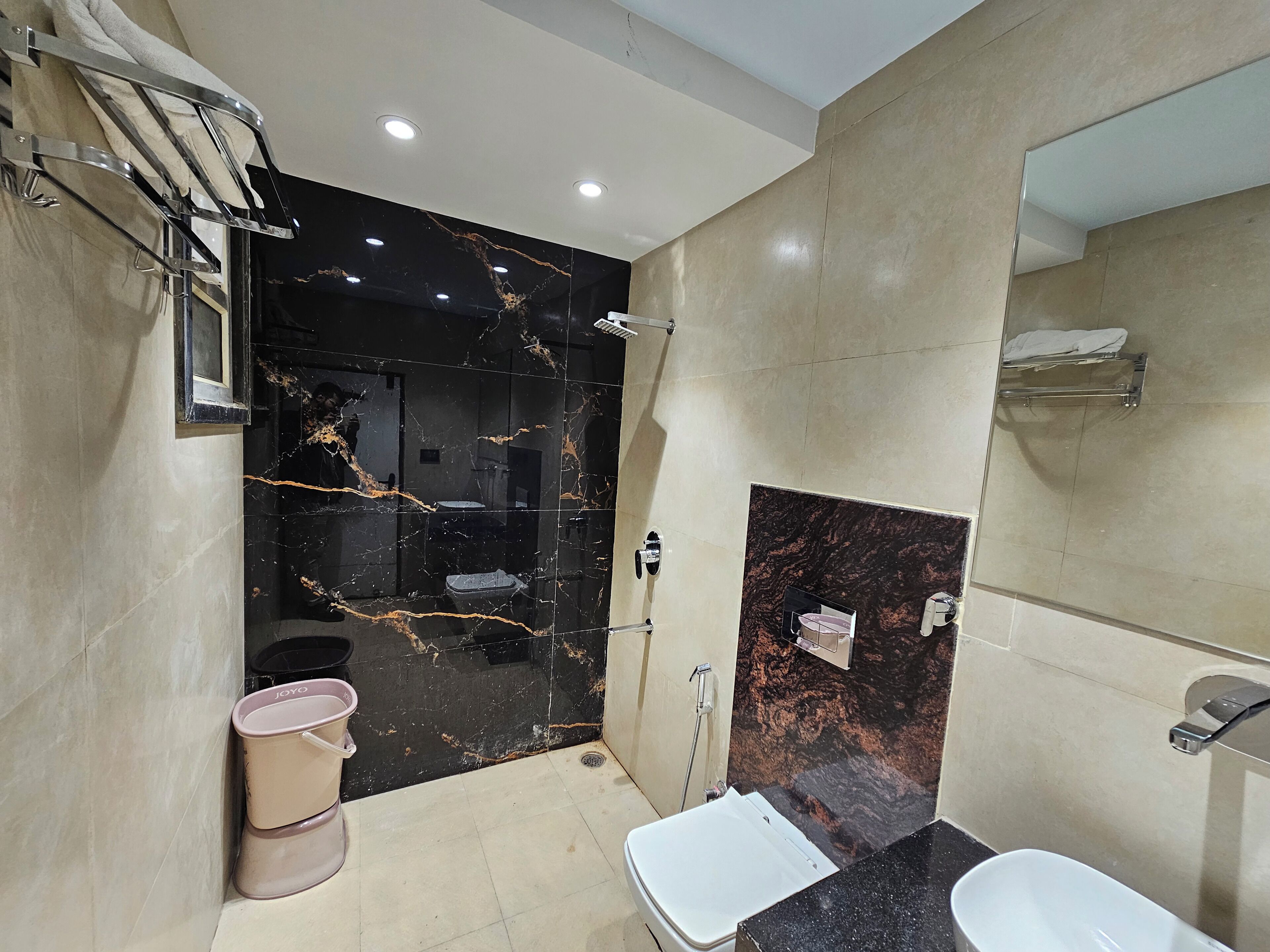 Un baño moderno con tocador de mármol negro, lavamanos blanco y zona de ducha.