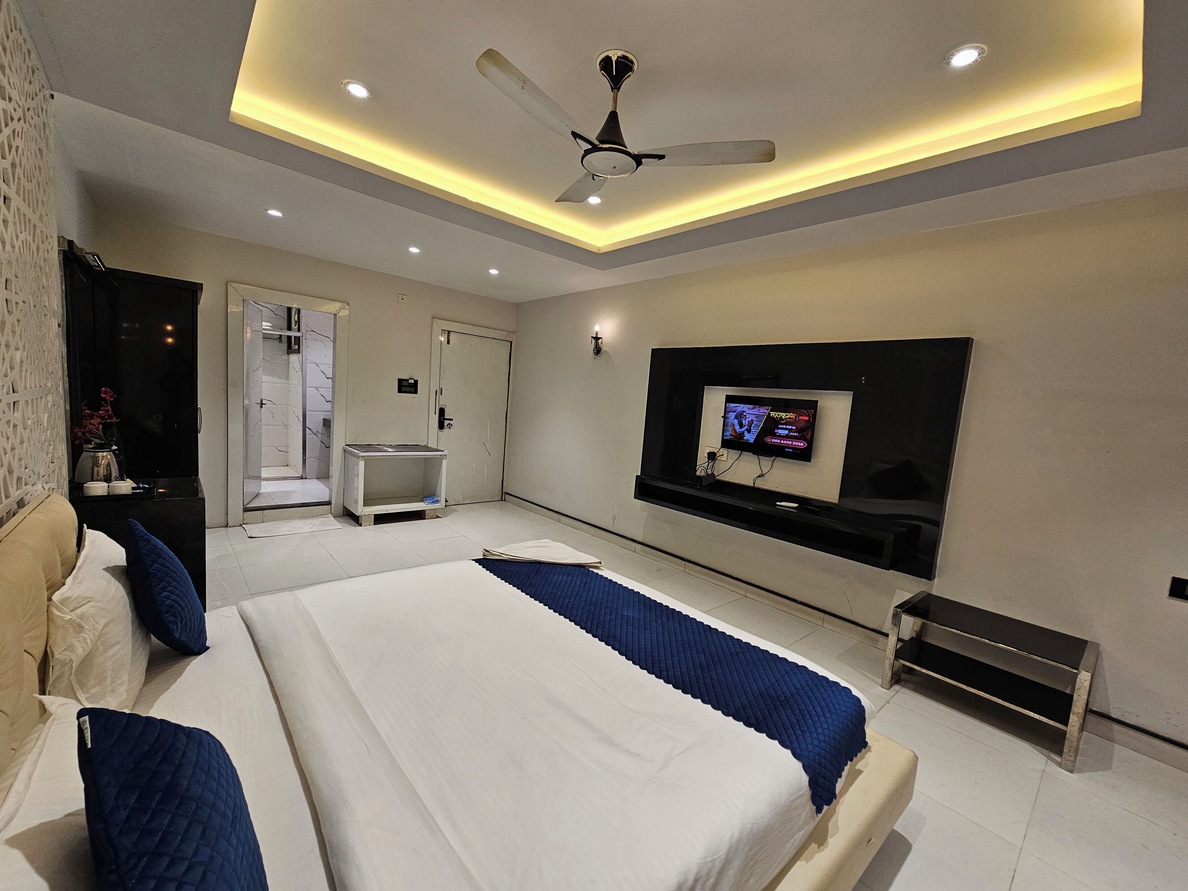 A modern bedroom with a large bed, a ceiling fan, recessed lighting, a TV, and a small bedside table.