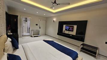A modern bedroom with a large bed, a ceiling fan, recessed lighting, a TV, and a small bedside table.