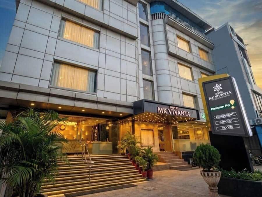 A multi-story hotel with a modern facade, a prominent entrance with steps, and signage indicating amenities like a restaurant, bar, and rooms.