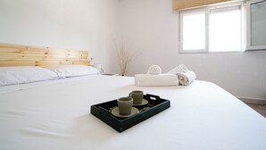 Cama bem arrumada com lençóis brancos, cabeceira de madeira e bandeja preta com duas xícaras e um prato.