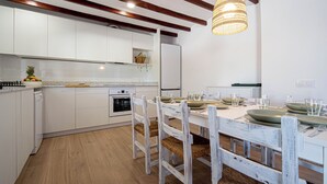 Cozinha moderna com armários brancos, vigas de madeira e um espaço de refeições com mesa e cadeiras brancas.