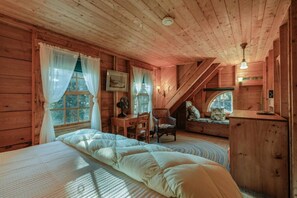 A cozy wooden cabin bedroom with a large bed, a desk, and a window seat.
