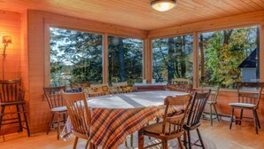 A wooden-paneled room with a large table and chairs, large windows, and a view of trees.