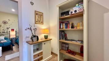 Un dormitorio con una cama, una mesita de noche con lámpara, un archivador pequeño y una estantería llena de libros y adornos.