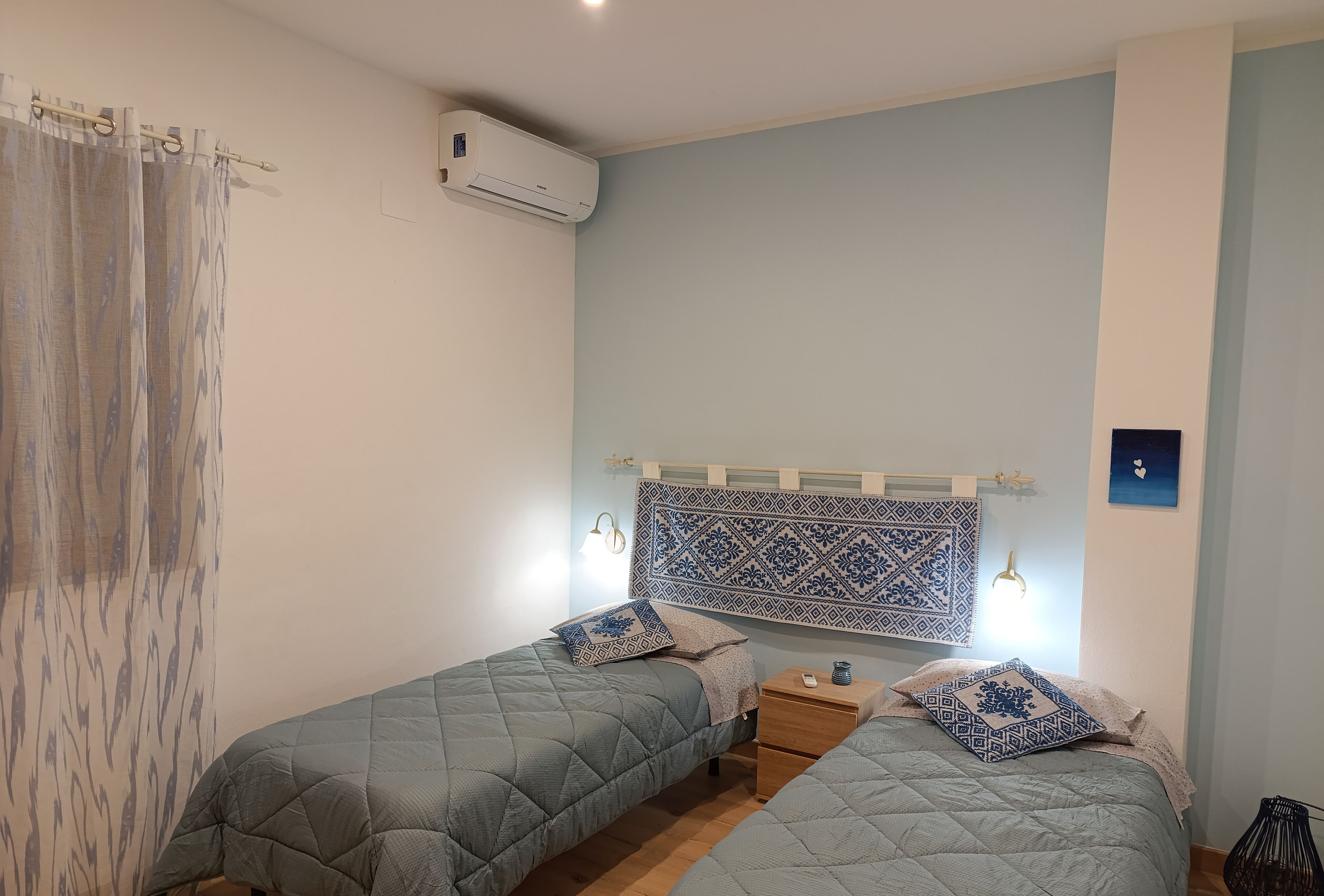 Une chambre avec deux lits, une tête de lit à motifs, des lampes de chevet et un appareil de climatisation.