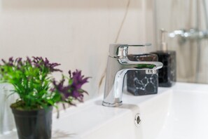 Une salle de bain moderne avec un robinet chromé, une plante en pot et un comptoir en marbre.