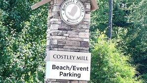 Kivipylväs, jossa on kyltti, joka osoittaa Costley Mill Beach -rannalle ja tapahtumien pysäköintialueelle.