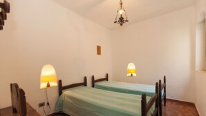 Un dormitorio con dos camas de madera, un escritorio pequeño y una silla. Hay dos lámparas de pared y una luz de techo.