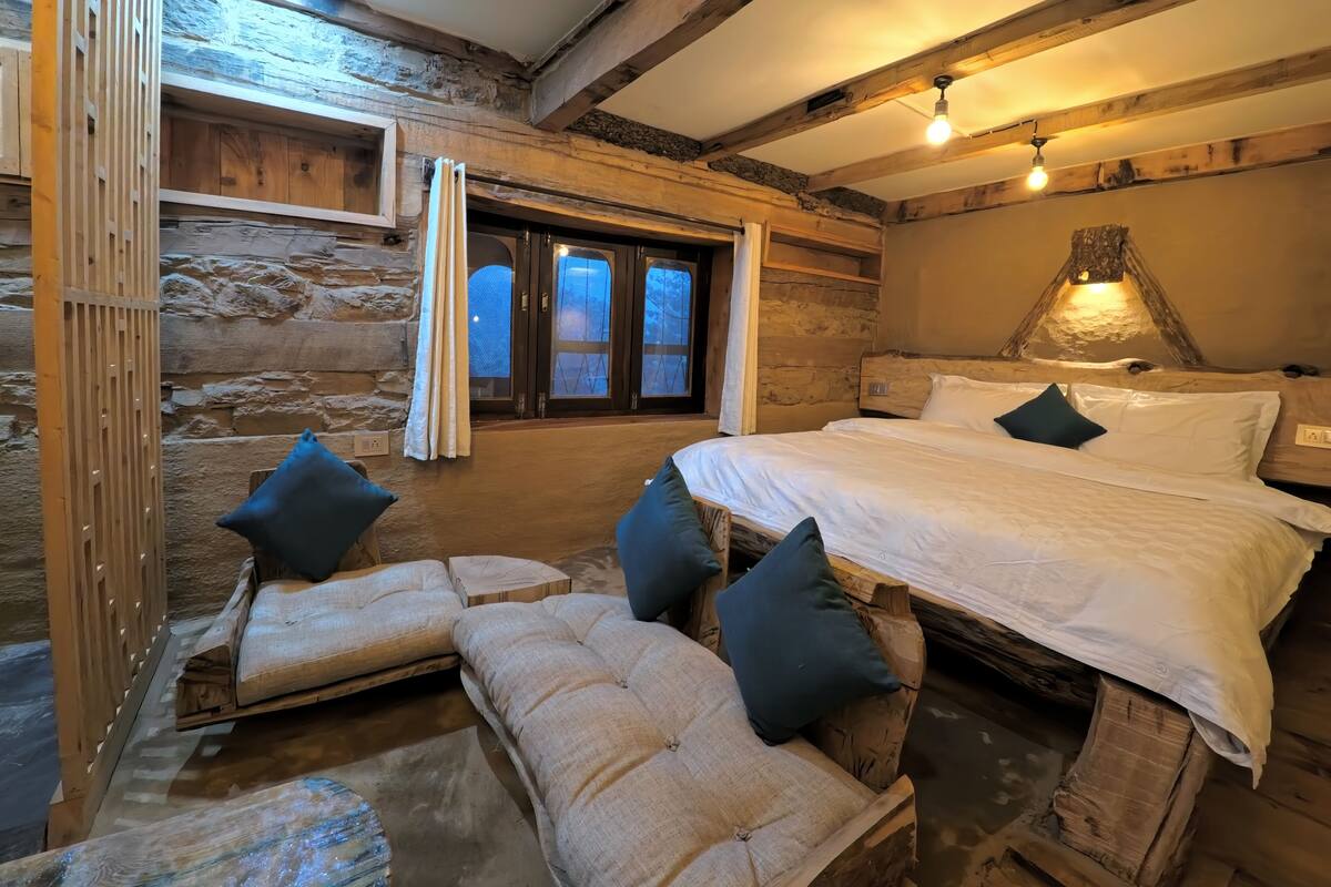 A rustic log cabin bedroom with a large bed, two sofas, and a stone wall.