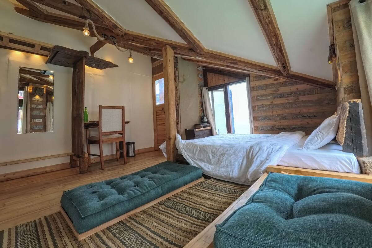 A rustic bedroom with exposed wooden beams, a bed, a bench, and a small table with a kettle.