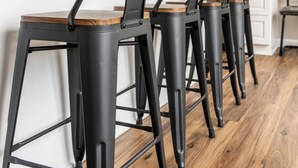 Una cocina con armarios blancos, encimera de granito y taburetes de metal negro.