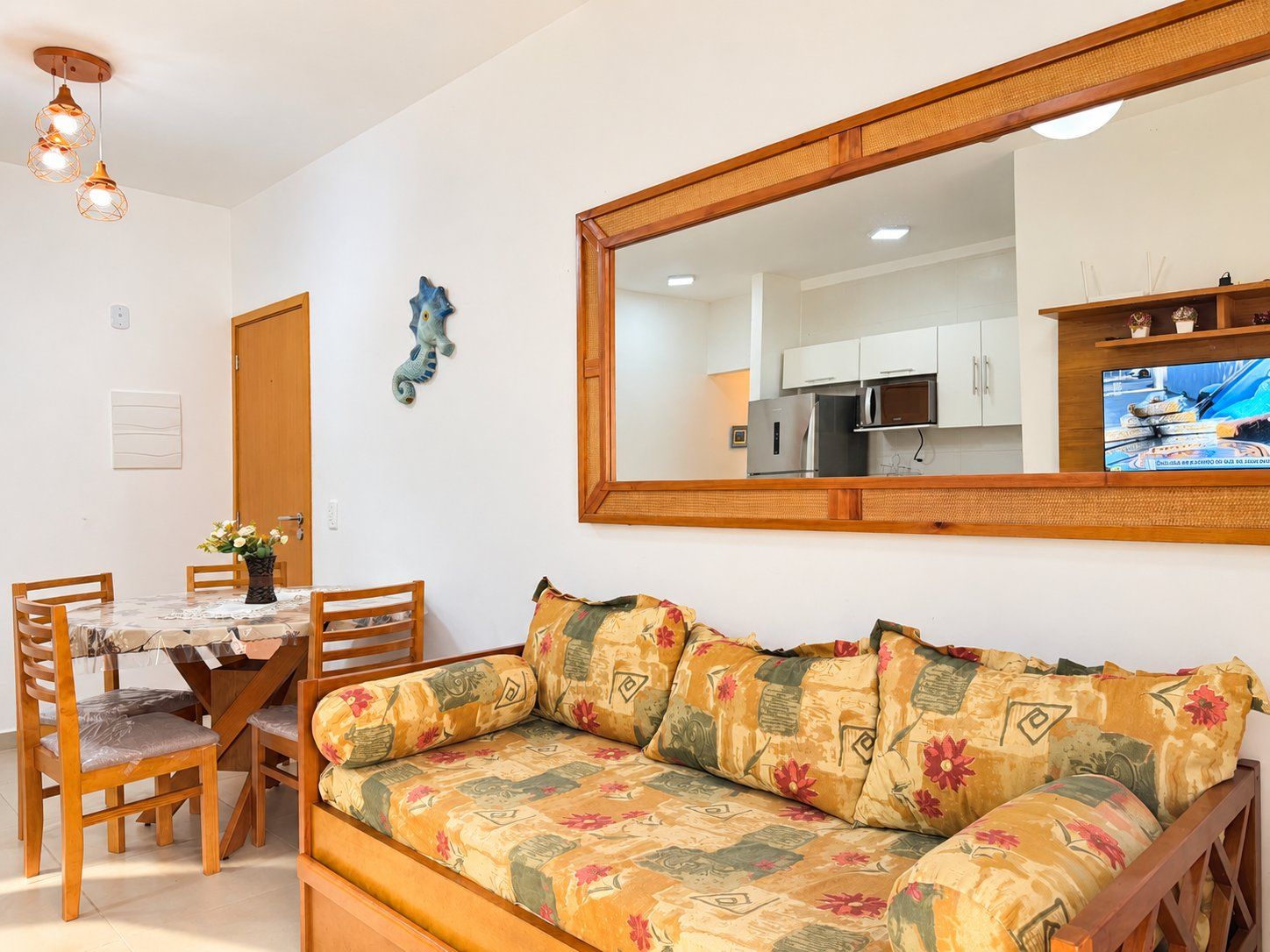 A living room with a sofa, a dining table with chairs, a mirror, and a kitchen area in the background.