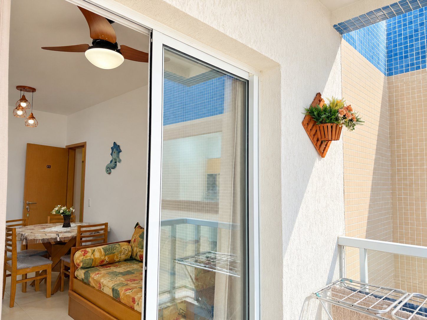 A room with a sliding glass door leading to a balcony, a ceiling fan, a dining table with chairs, and a hanging plant.