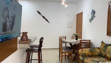 Un soggiorno con divano, tavolo da pranzo con sedie, televisore a parete e lampadario.