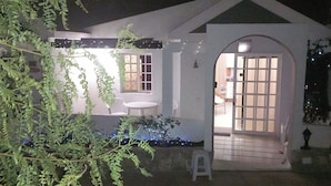 Um edifício com fachada branca, um pequeno alpendre com uma cadeira branca e uma porta que dá para o interior.