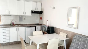Uma cozinha compacta com armários brancos, pia, pequeno frigorífico e área de refeições com mesa e cadeiras.
