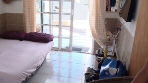 Quarto pequeno e limpo com cama, uma mesa com uma caneca e uma janela com cortinas.