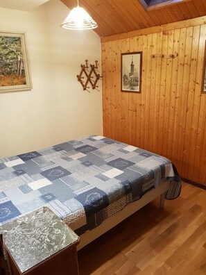 A room with wooden panel walls, a bed with a quilt, a hanging light fixture, and a framed picture on the wall.