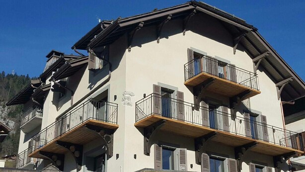 Un edificio a più piani con balconi, un tetto spiovente e uno sfondo montuoso.