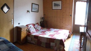 Una stanza con un letto, un piccolo comò in legno, una scrivania con una sedia e una finestra con tende.