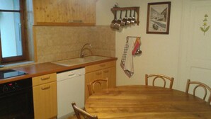 Una cucina con mobili in legno, un lavello, una lavastoviglie e un tavolo da pranzo con sedie. Una finestra si trova sul lato sinistro.
