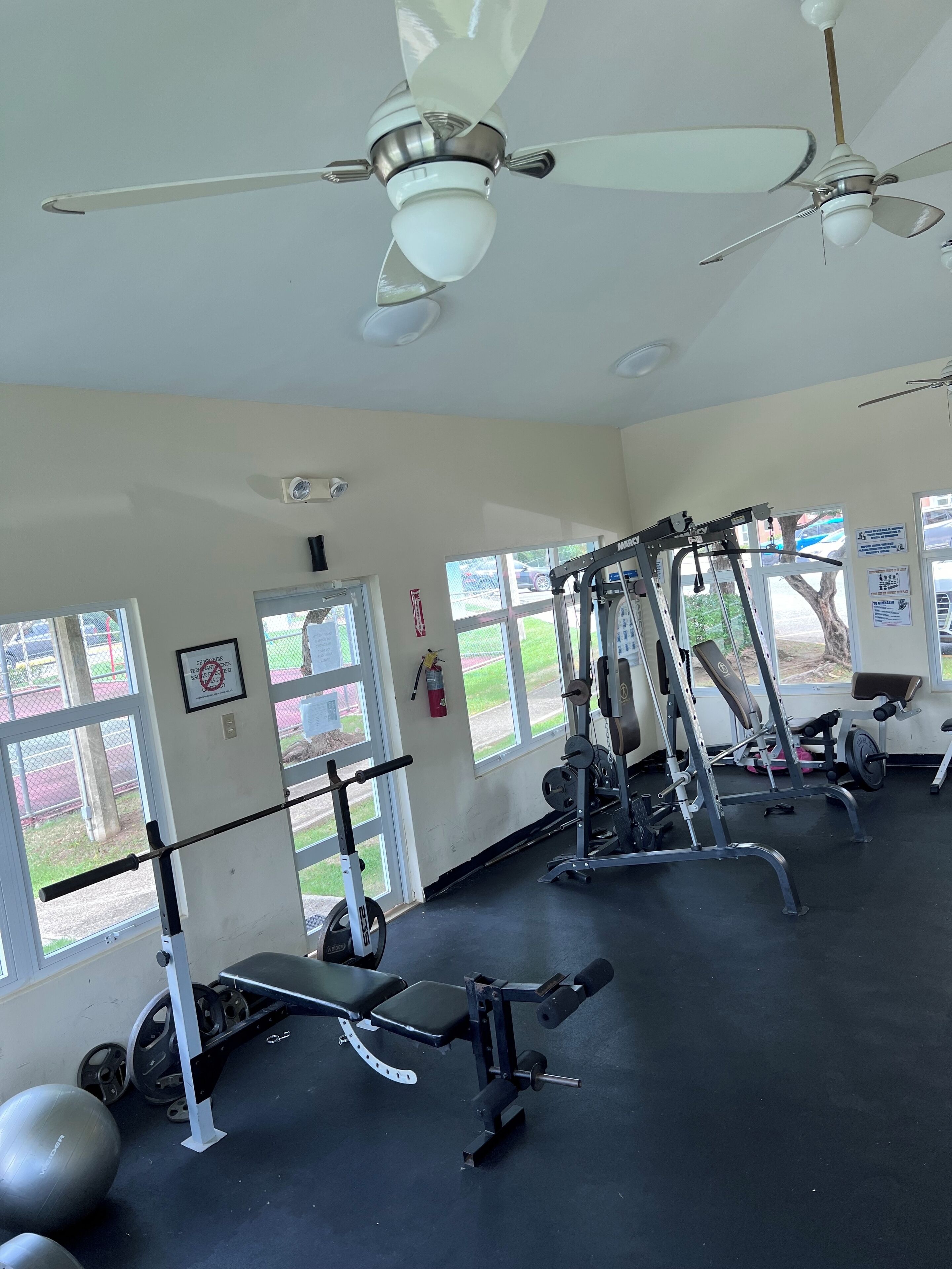 A gym with ceiling fans, exercise equipment, and large windows.
