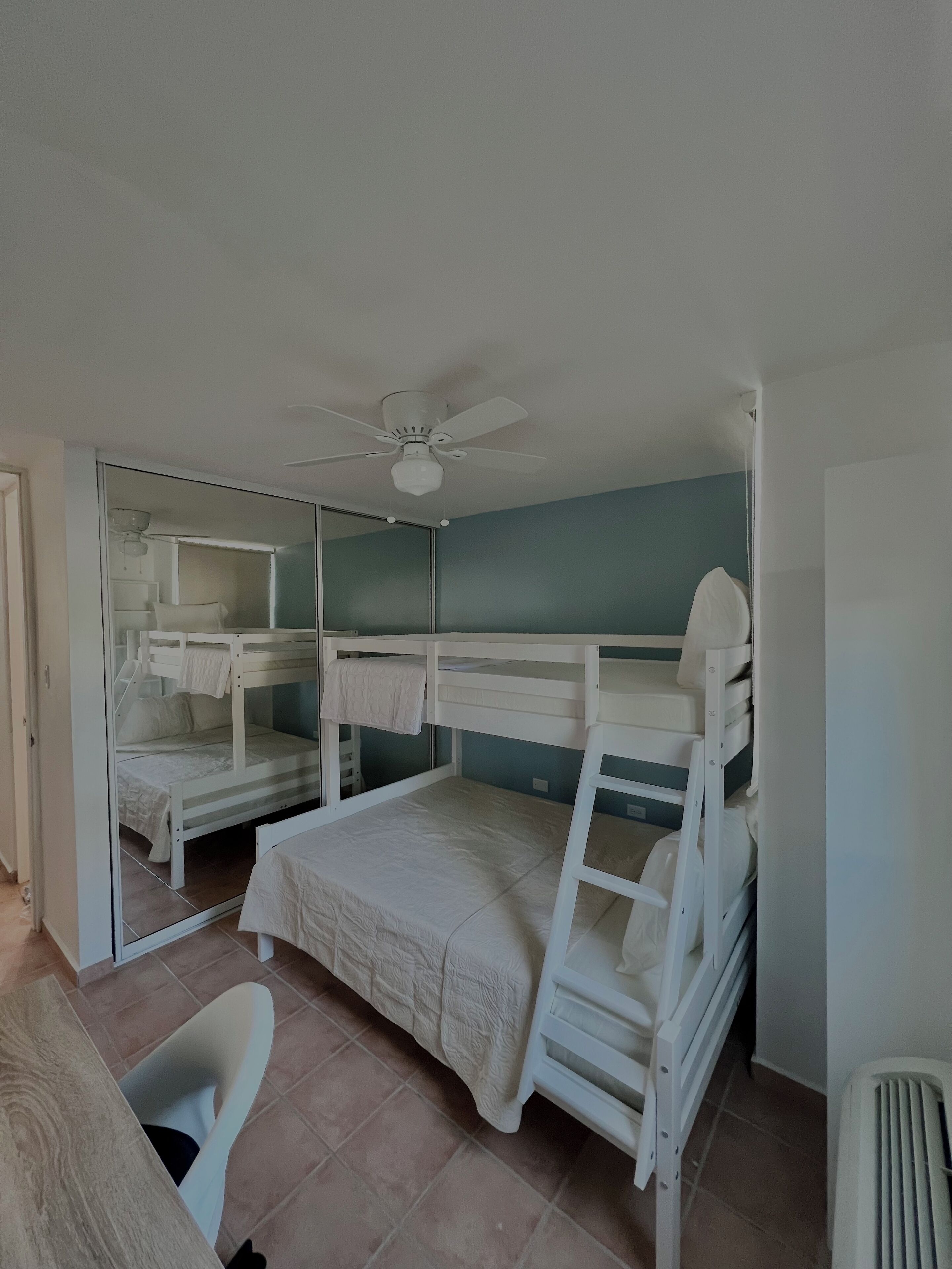 Une chambre avec des lits superposés, un ventilateur de plafond, un miroir et une chaise.
