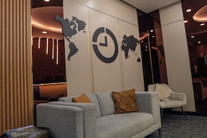 Un hall d’entrée moderne avec un canapé gris, une carte du monde et une horloge.