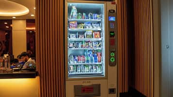 Máquina automática com variedade de lanches e bebidas, interface de pagamento e um botão.
