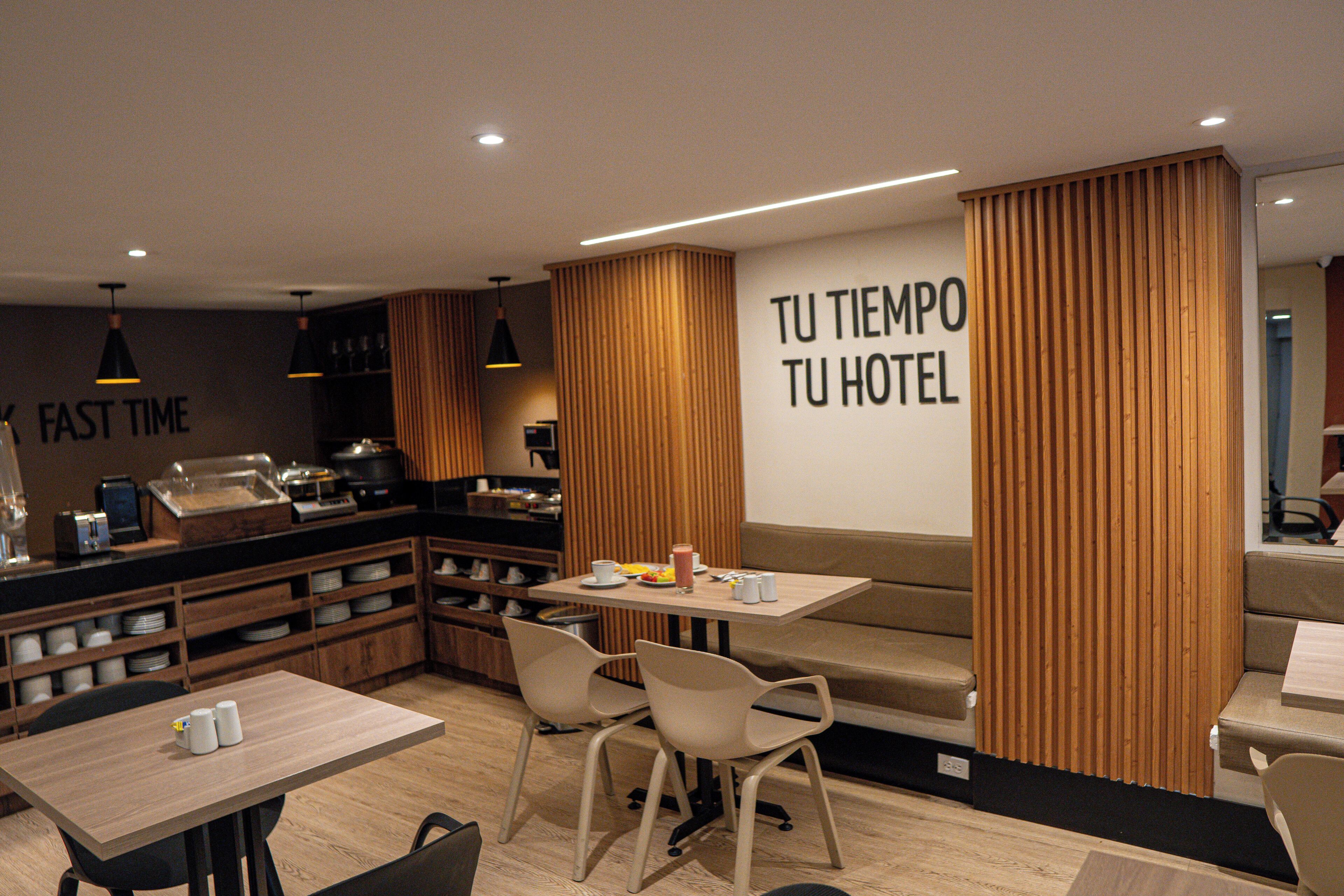 A modern hotel lobby with a seating area, a counter with a coffee machine, and a wall with a motivational message.